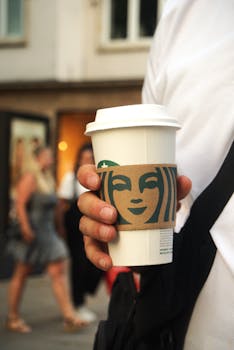 Close-up of a hand holding a coffee cup on a bustling street in Stuttgart, Germany.