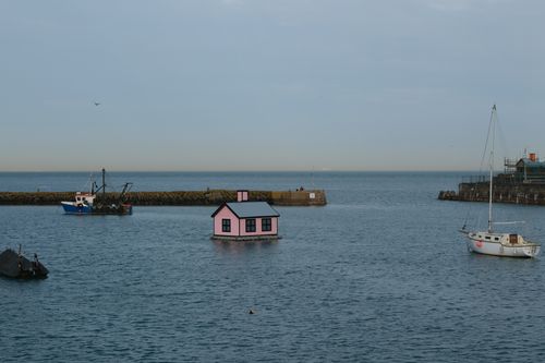 Free A unique pink house floats in a peaceful harbor with boats under a clear sky. Stock Photo