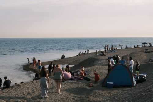 Free A bustling beach scene with people enjoying summer by the sea at sunset. Stock Photo