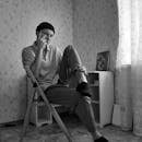 一名男子悠闲地坐在房间的椅子上，摆出姿势，画面是黑白的