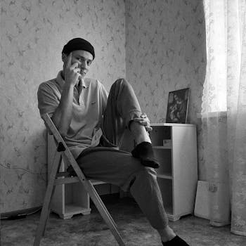 一名男子悠闲地坐在房间的椅子上，摆出姿势，画面是黑白的
