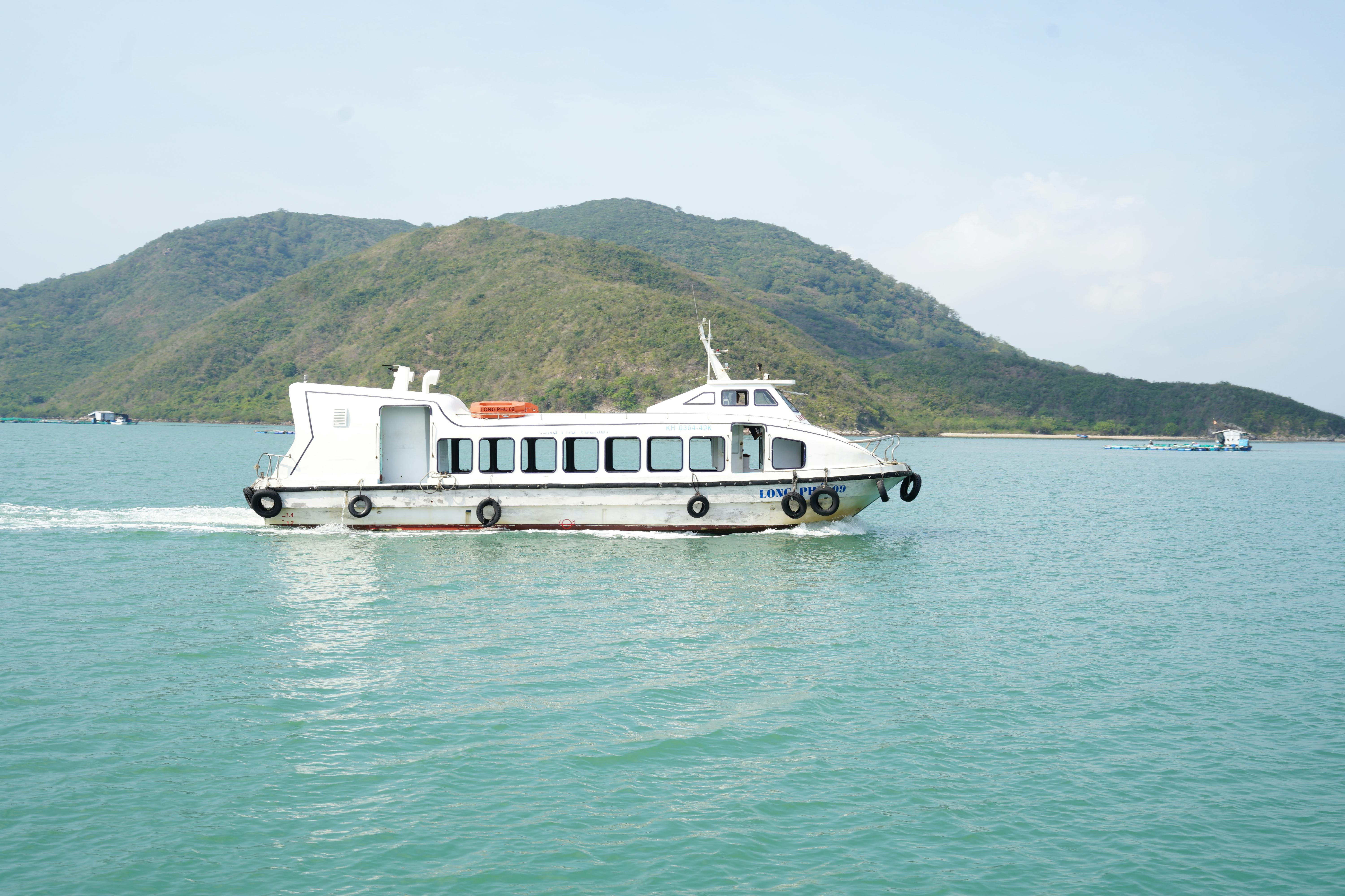 White ferry boat cruising on a serene lake with green hills in the background on a sunny day.