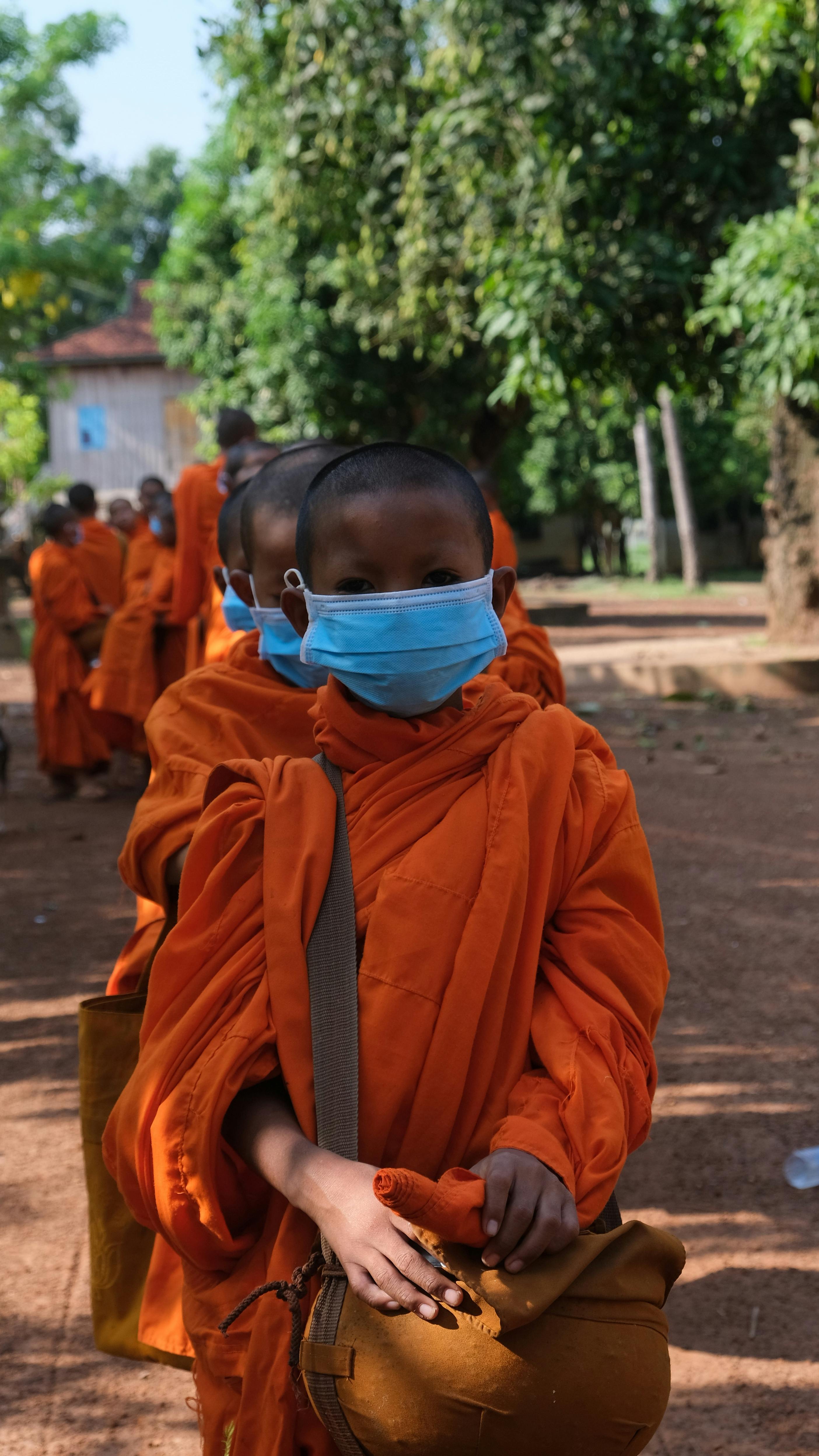 A line of young Buddhist monks wearing face masks, highlighting health precautions in Cambodia.