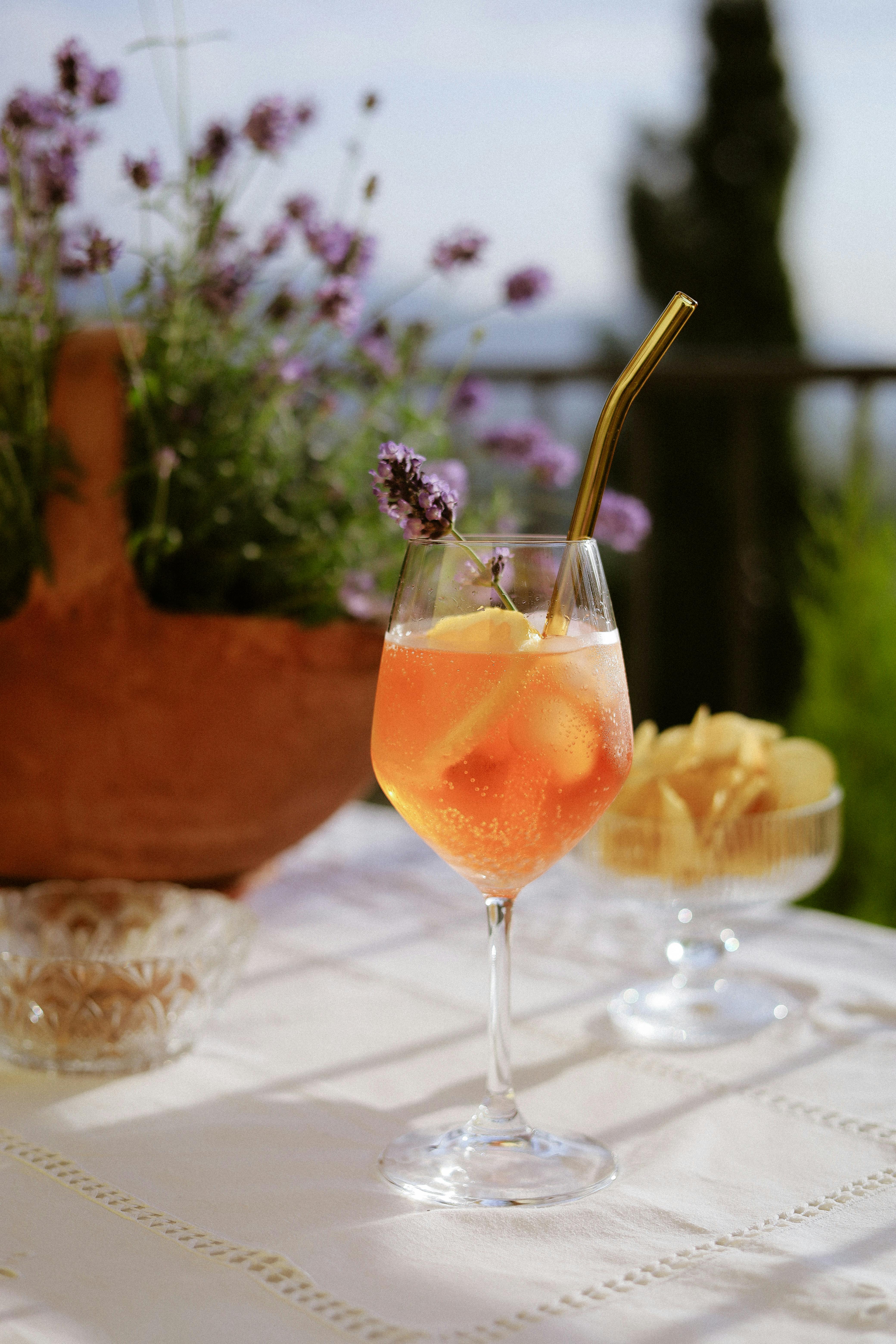 Chilled Aperol Spritz with lemon slice and straw, set on a sunny patio table surrounded by lavender.
