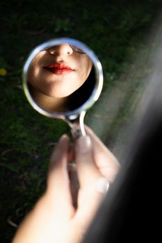 A woman's lips with red lipstick reflected in a hand mirror.