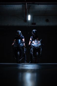 Two motorcyclists with helmets feature prominently in a dimly lit garage, exuding a sense of adventure.