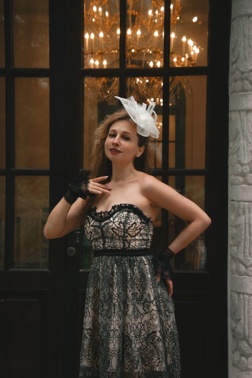 Free Stylish woman in a lace dress and fascinator standing indoors, exuding elegance and charm. Stock Photo