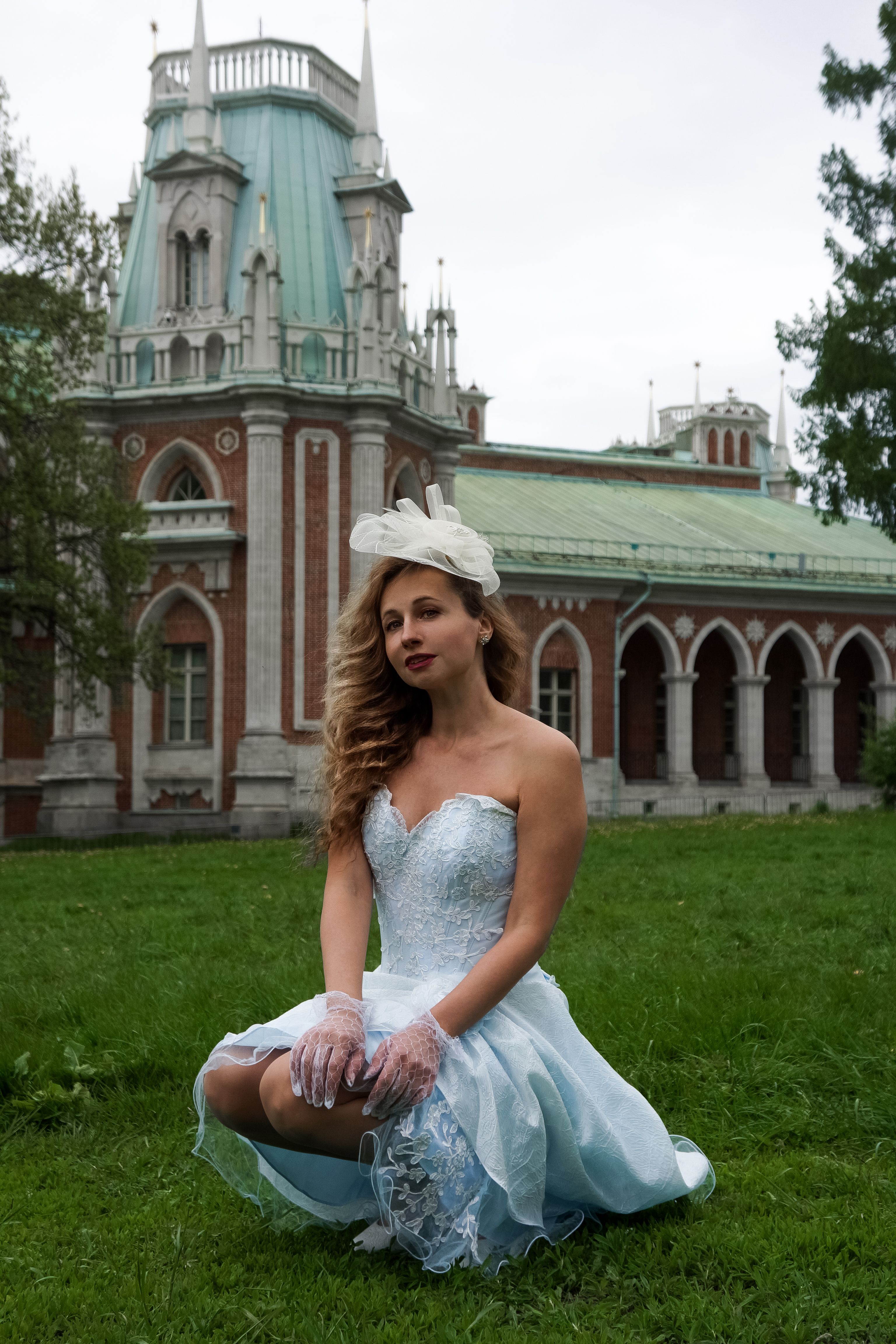 Stylish woman in vintage dress and hat posing in front of historic architecture.