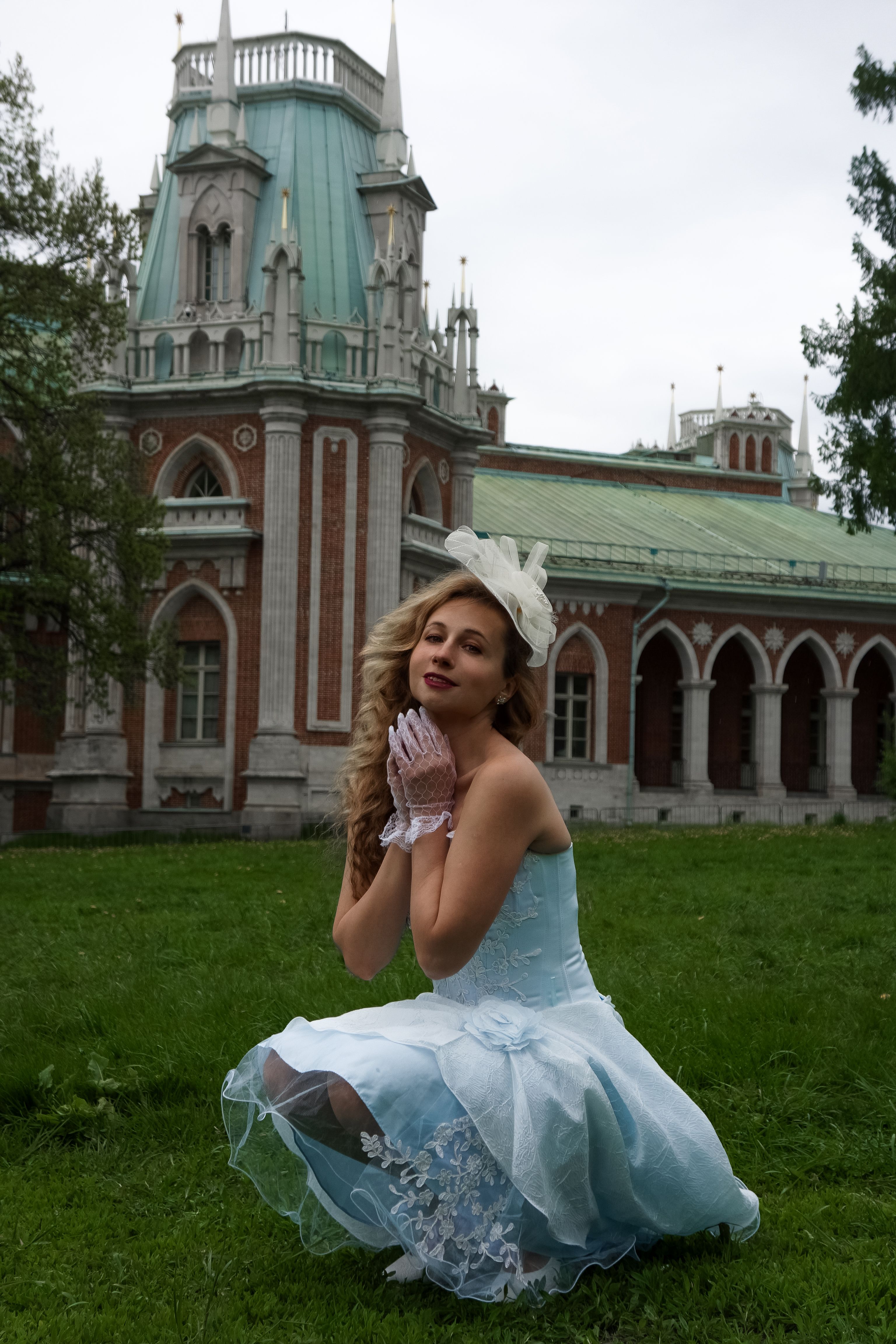 Elegant woman in vintage blue dress poses near a historic building with Gothic architecture.
