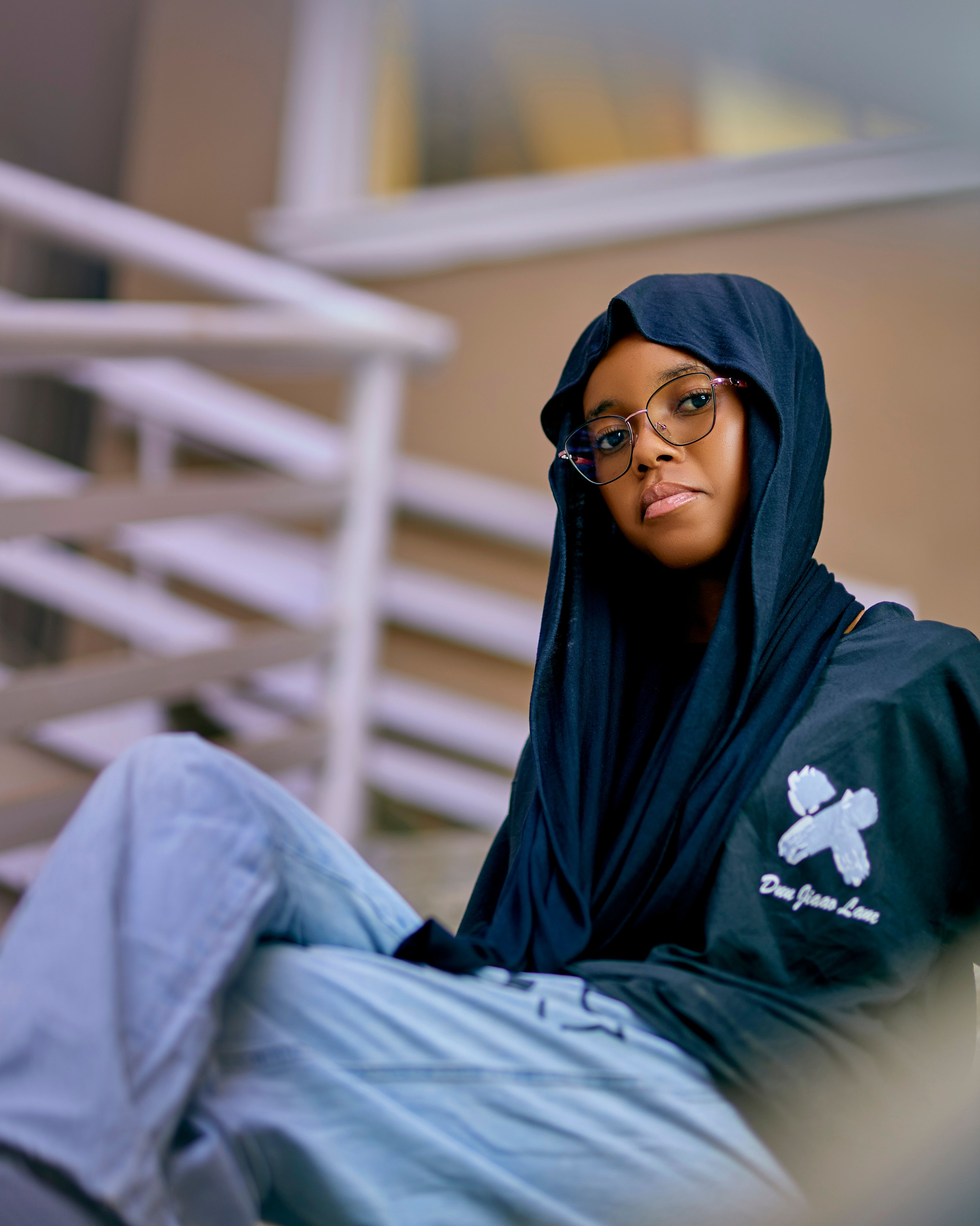 A young woman wearing glasses and a hijab in a modern, stylish setting indoors.