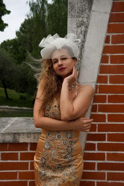 Free Fashionable woman in a stylish dress with white accessories posing outdoors against a brick wall. Stock Photo
