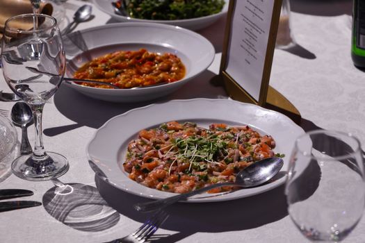 A sophisticated dinner setup featuring a dish of salmon tartare garnished with greens.