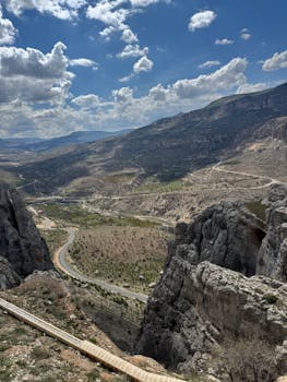 Breathtaking panorama of a rugged mountain landscape with winding road and dramatic cliffs under a cloudy sky.