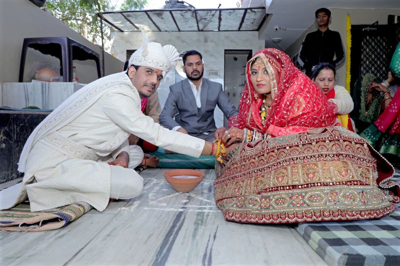 Bride and groom in traditional attire during an Indian wedding ritual indoors.