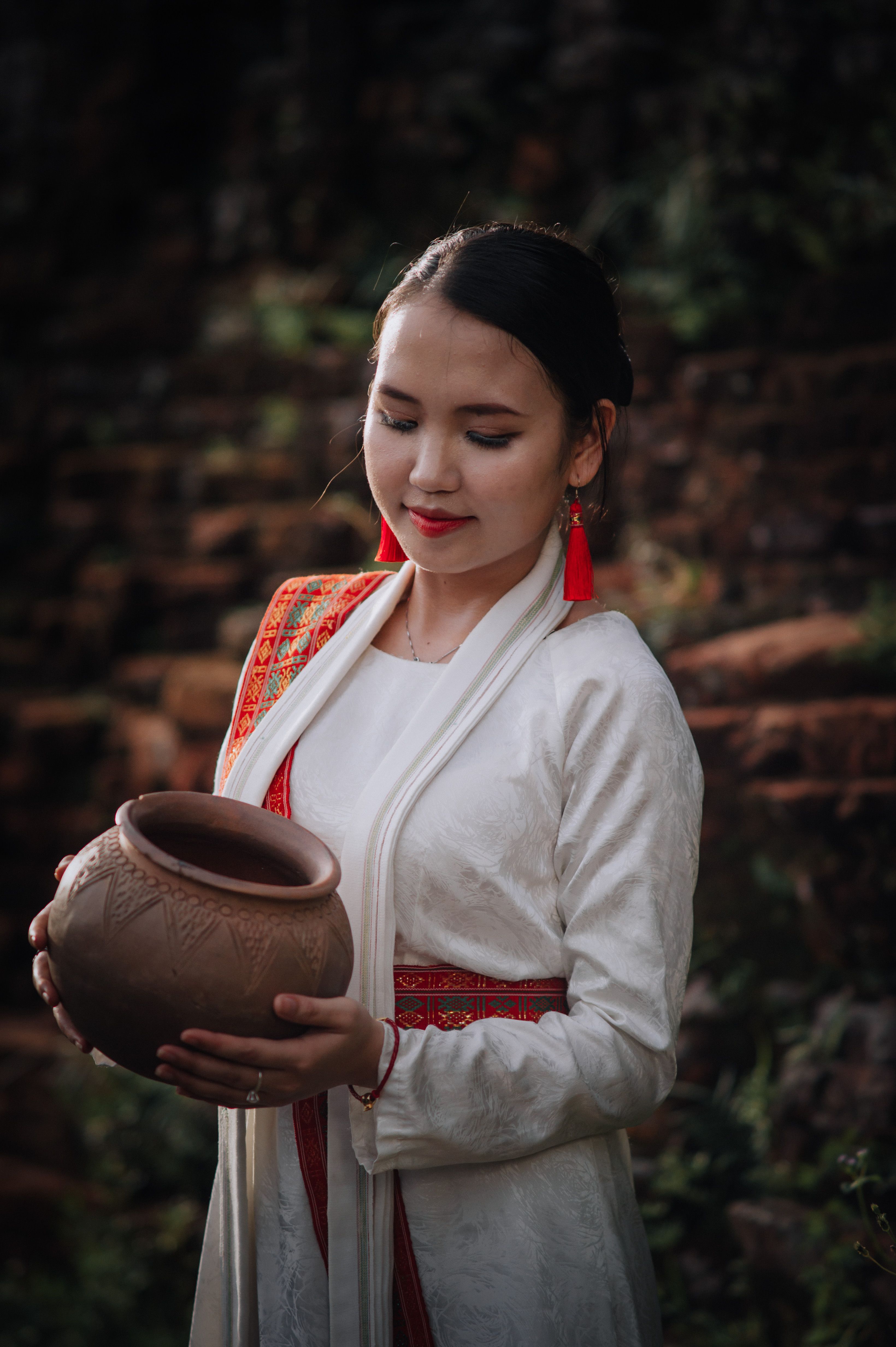 A woman in traditional attire gracefully holds an earthen pot. Captured with a warm and artistic style.