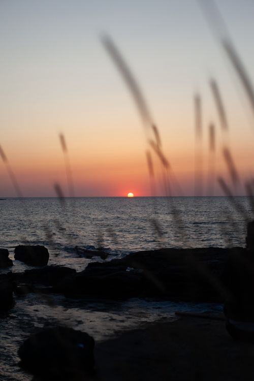 Free Peaceful sunset on the ocean with silhouettes of rocks and distant grass, creating a tranquil atmosphere. Stock Photo