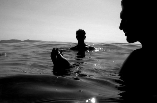 Two silhouetted figures swimming in the ocean, captured at daytime with a serene horizon.