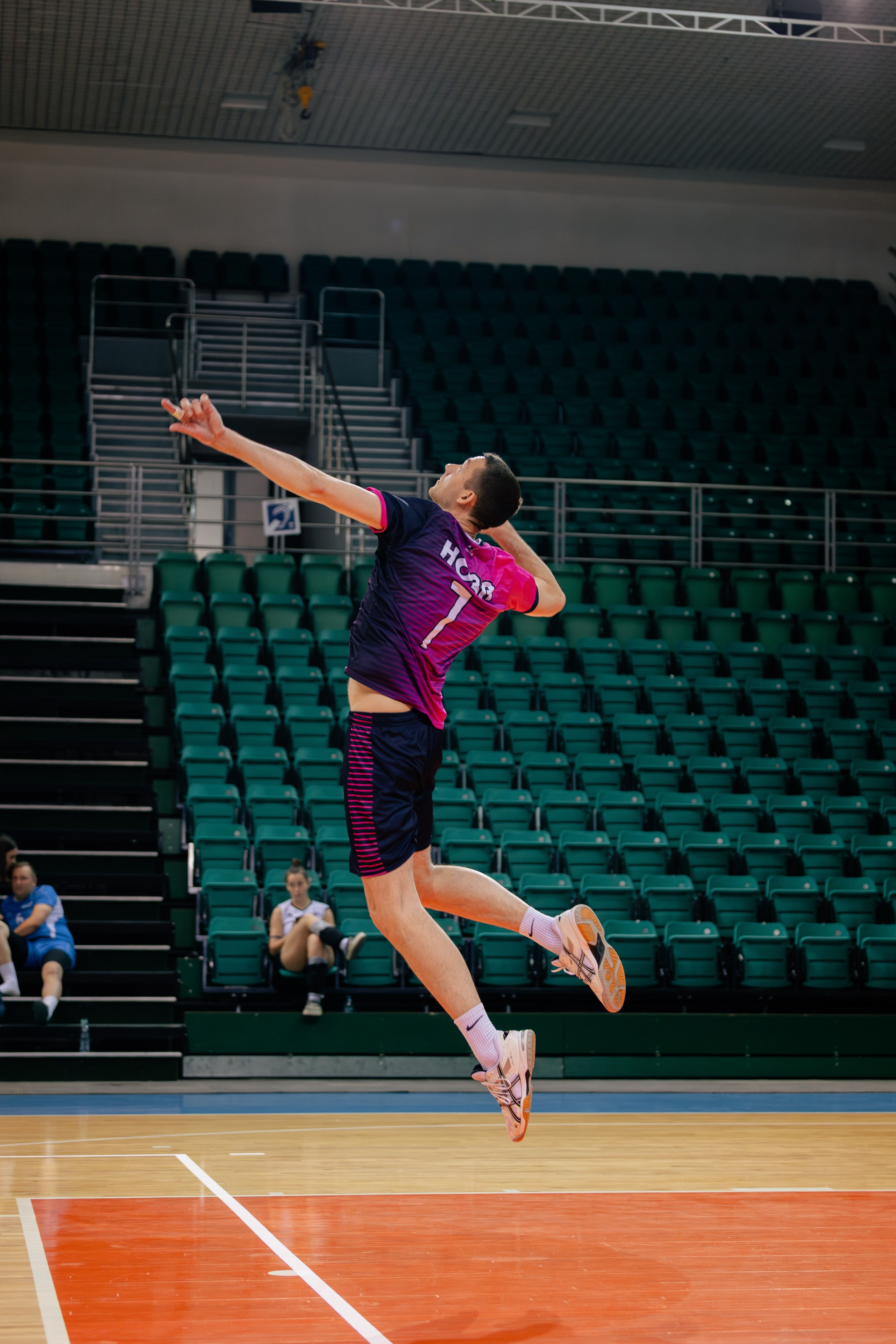 Dynamic image of a male volleyball player executing a high jump serve in an indoor arena.