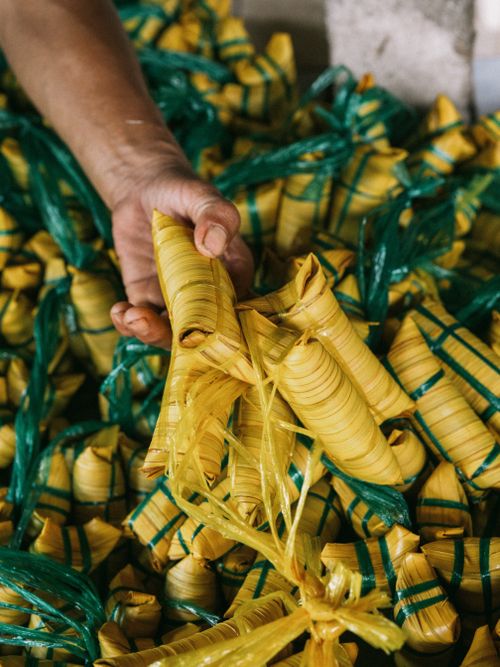 Free Hand selecting traditional banana leaf wrapped food bundles, showcasing cultural packaging. Stock Photo