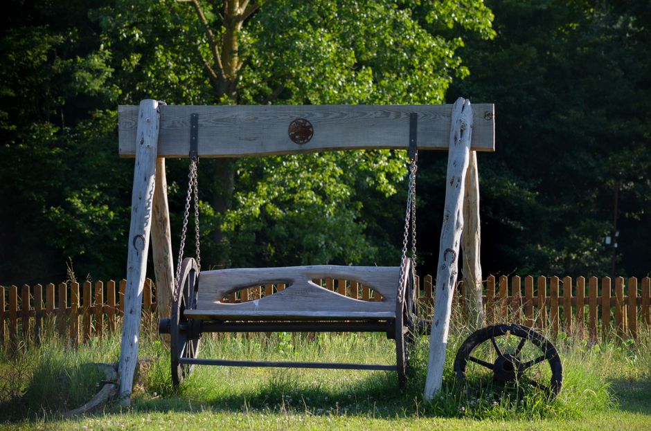 Charming wooden swing in a lush green backyard, perfect for relaxation.
