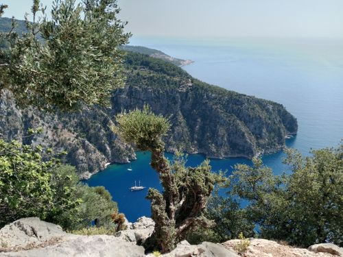 Free A breathtaking view of the Mediterranean coast featuring lush cliffs and a sailboat in clear blue waters. Stock Photo