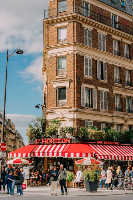Lively street scene in Paris with L'Horizon cafe and classic architecture under a bright blue sky.