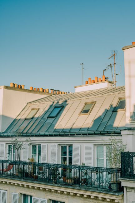 Elegant Parisian building with traditional rooftops and chimneys under a bright blue sky.