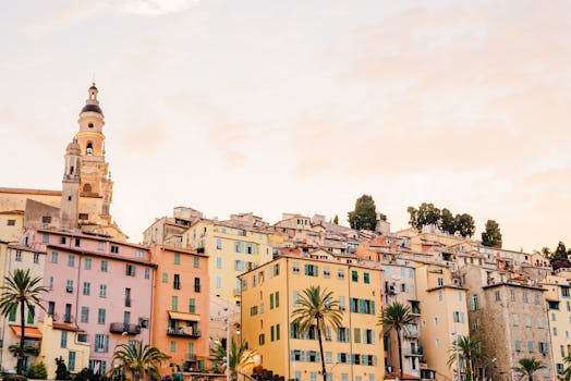 Bright, pastel houses and a historic church in Menton, France, at sunset.