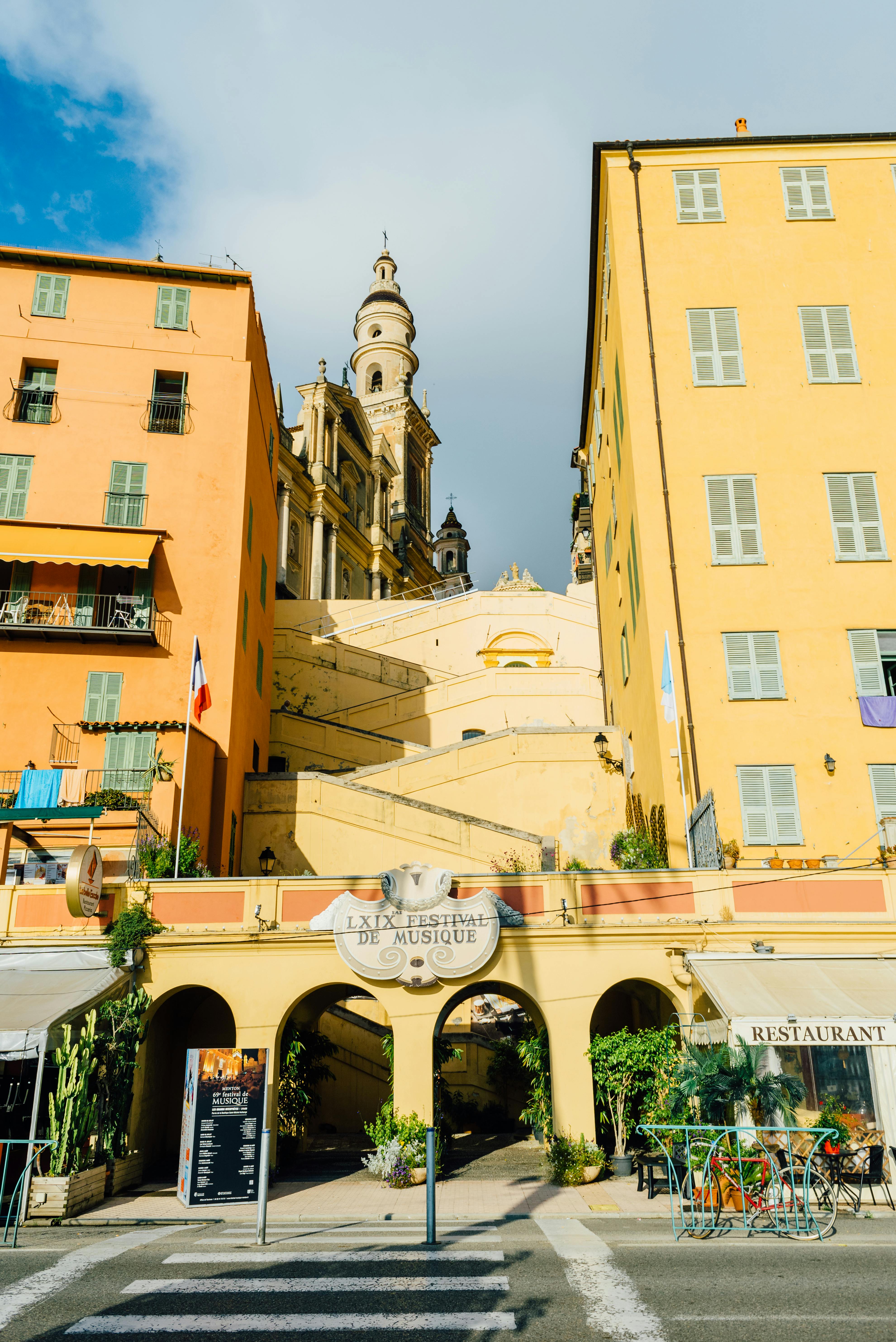 Colorful buildings line a street with St. Michel's Basilica in sunny Menton, France.