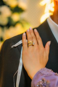 Close-up of a bride's hand with a golden ring resting on the groom's shoulder.