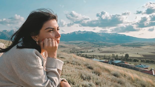 Young woman gazing thoughtfully at scenic mountains under a blue sky.
