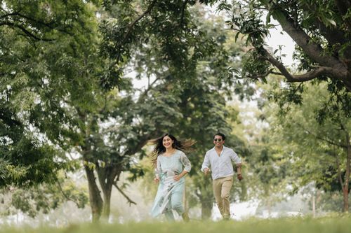 Free A cheerful couple enjoys a playful run through a lush, green park, surrounded by trees and nature. Stock Photo