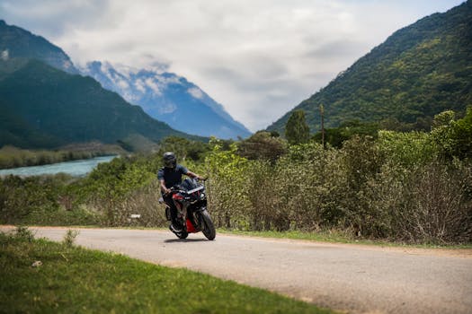 A motorcyclist navigates a winding road through lush green mountains, under a cloudy sky.