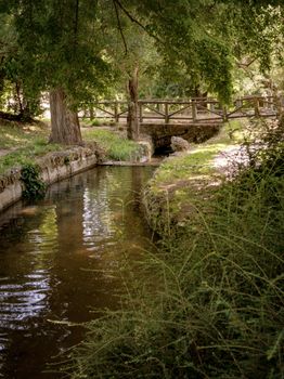 Peaceful stream under a wooden bridge surrounded by greenery in a Madrid park during summer day.