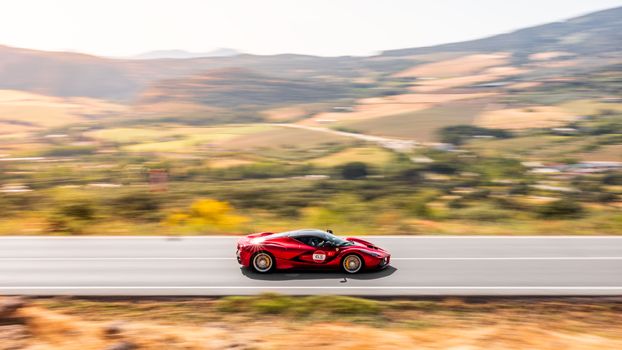 A vibrant red sports car speeds down a highway through a picturesque landscape.