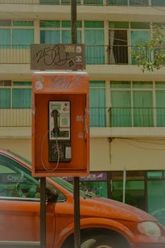 A red payphone on a street in Zacatecas, Mexico against an urban backdrop.