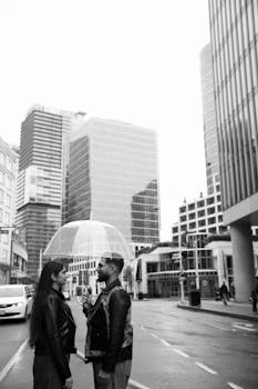 A couple under an umbrella on a city street, surrounded by tall buildings.