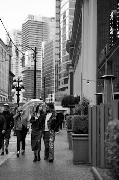 Monochrome photo of a couple walking with an umbrella in a modern city setting.
