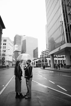 A couple sharing an umbrella in a rainy city street surrounded by skyscrapers.