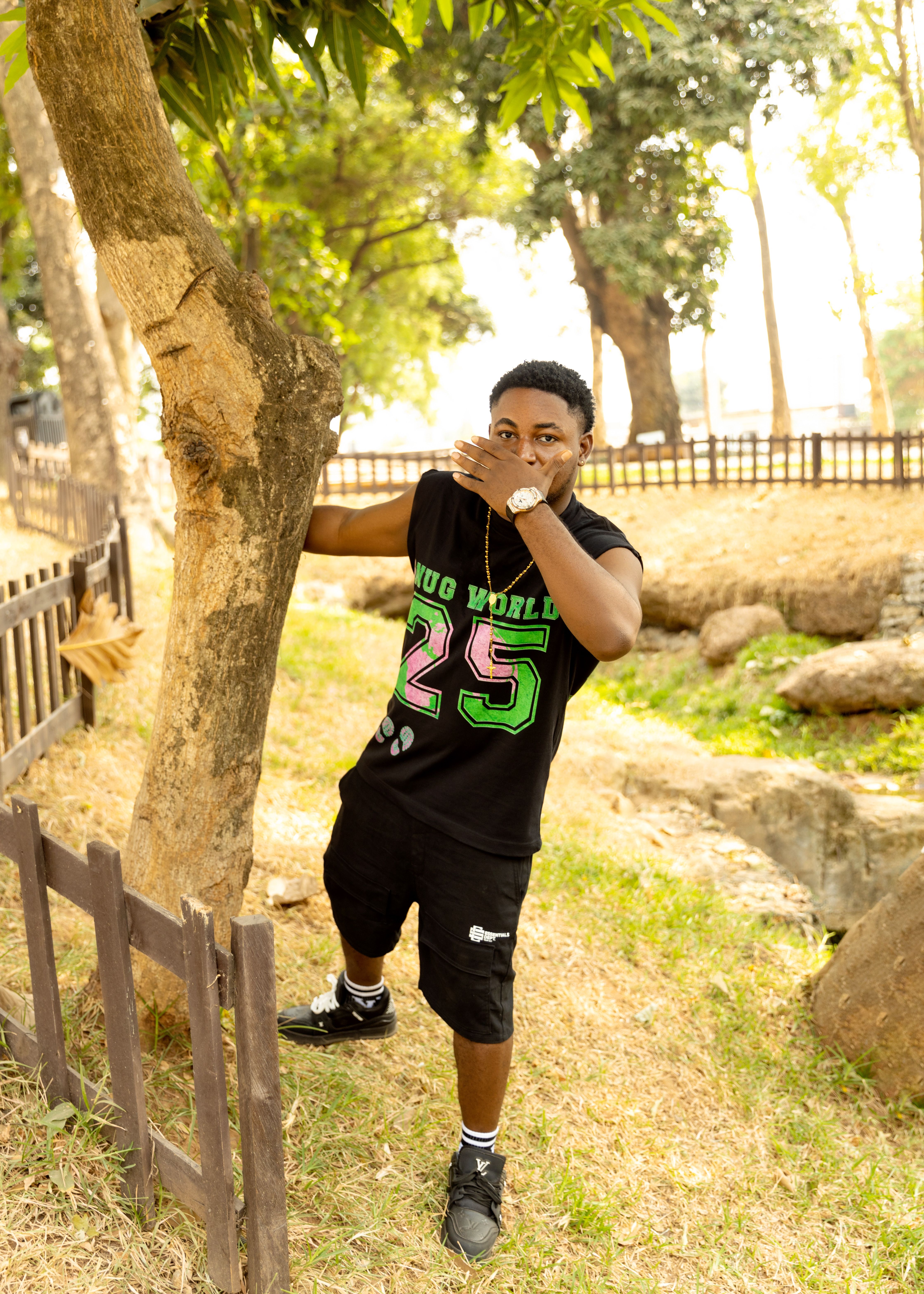 Young man in casual attire playfully interacts with a tree in a sunny park.