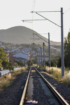 Scenic railway tracks leading to a picturesque hilltop town at sunset.
