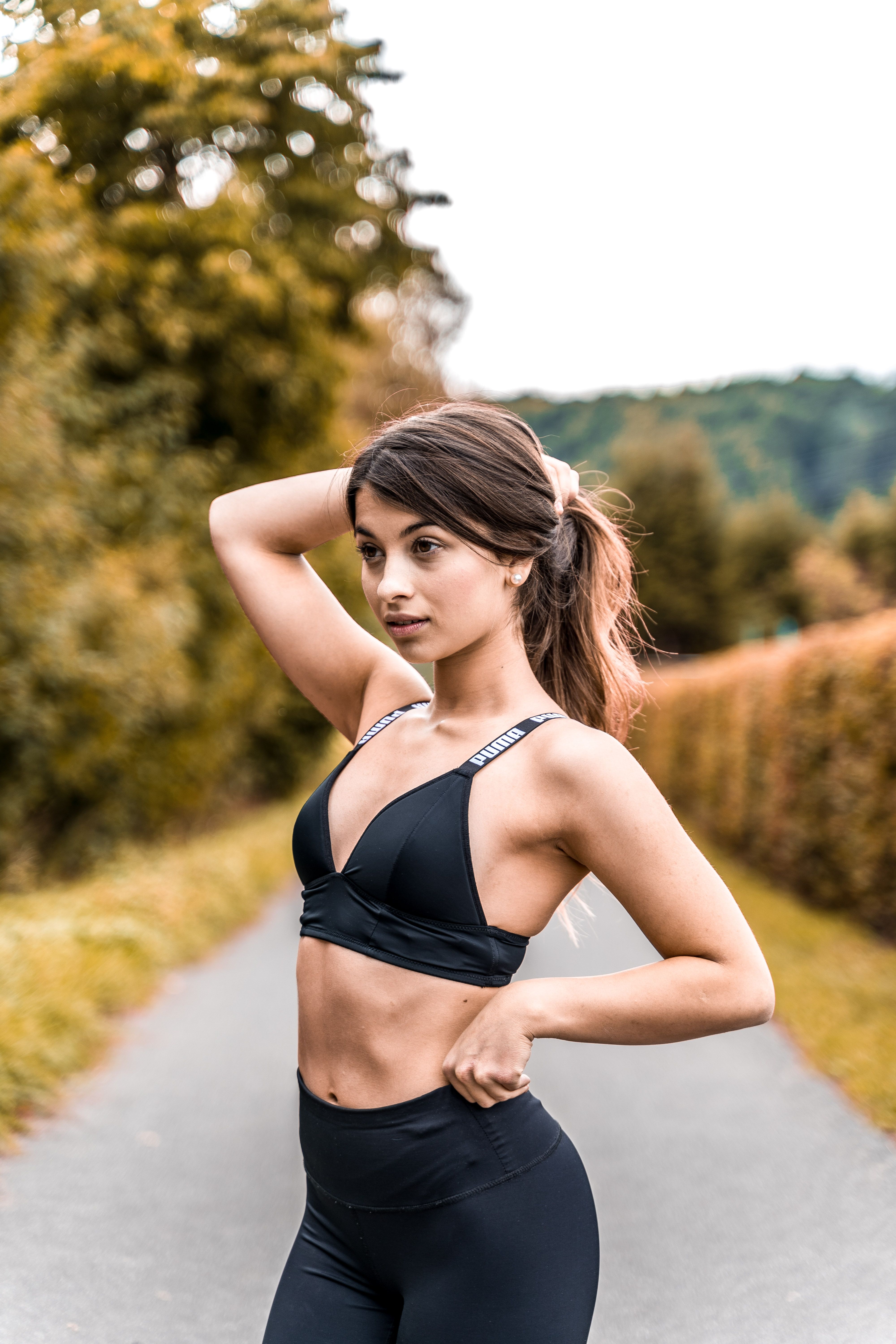 Fit woman posing on a scenic country road, showcasing athletic wear and healthy lifestyle.