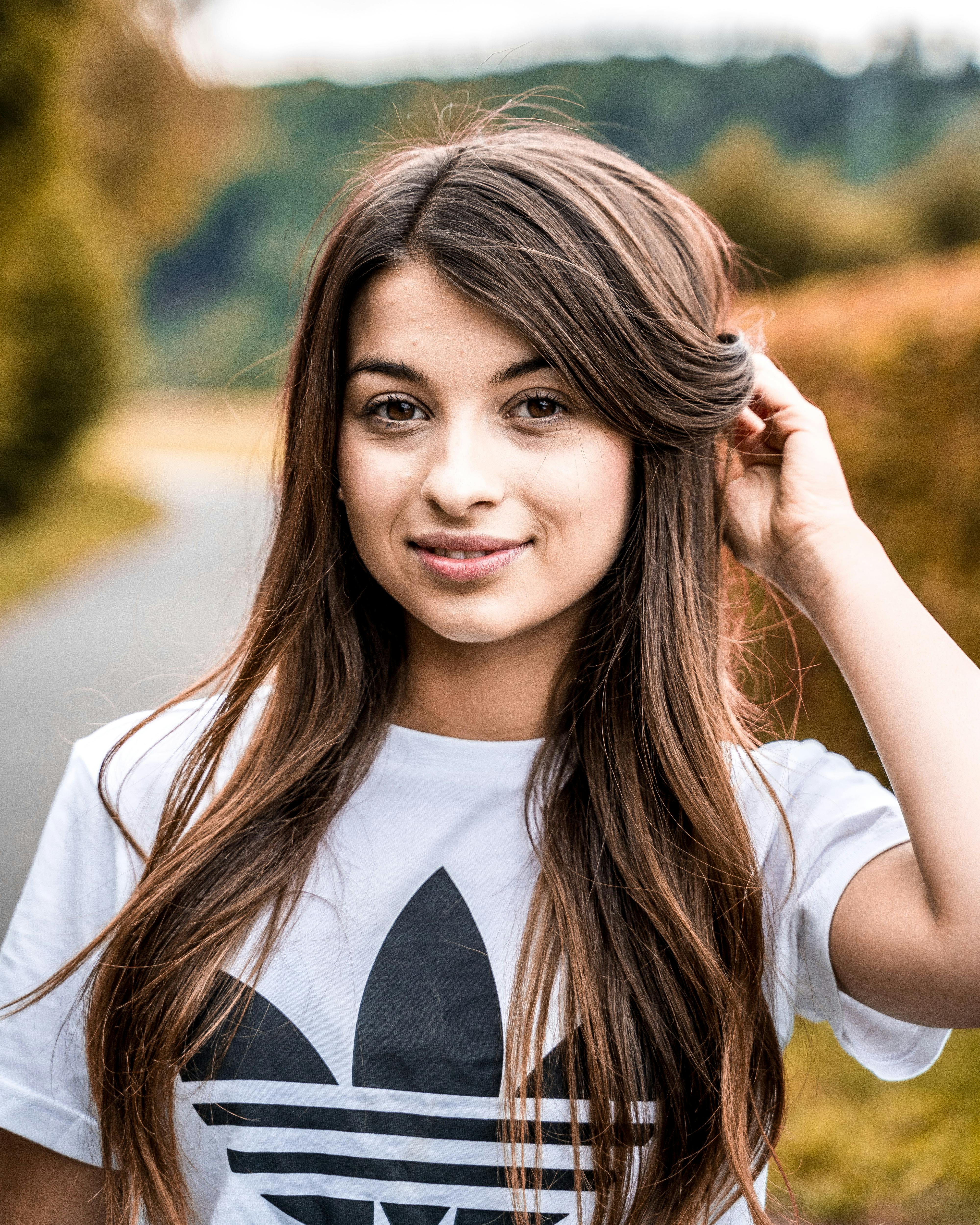 一位面带微笑的黑发女子穿着白衬衫，在户外享受着阳光明媚的一天，摆出姿势