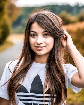 一位面带微笑的黑发女子穿着白衬衫，在户外享受着阳光明媚的一天，摆出姿势