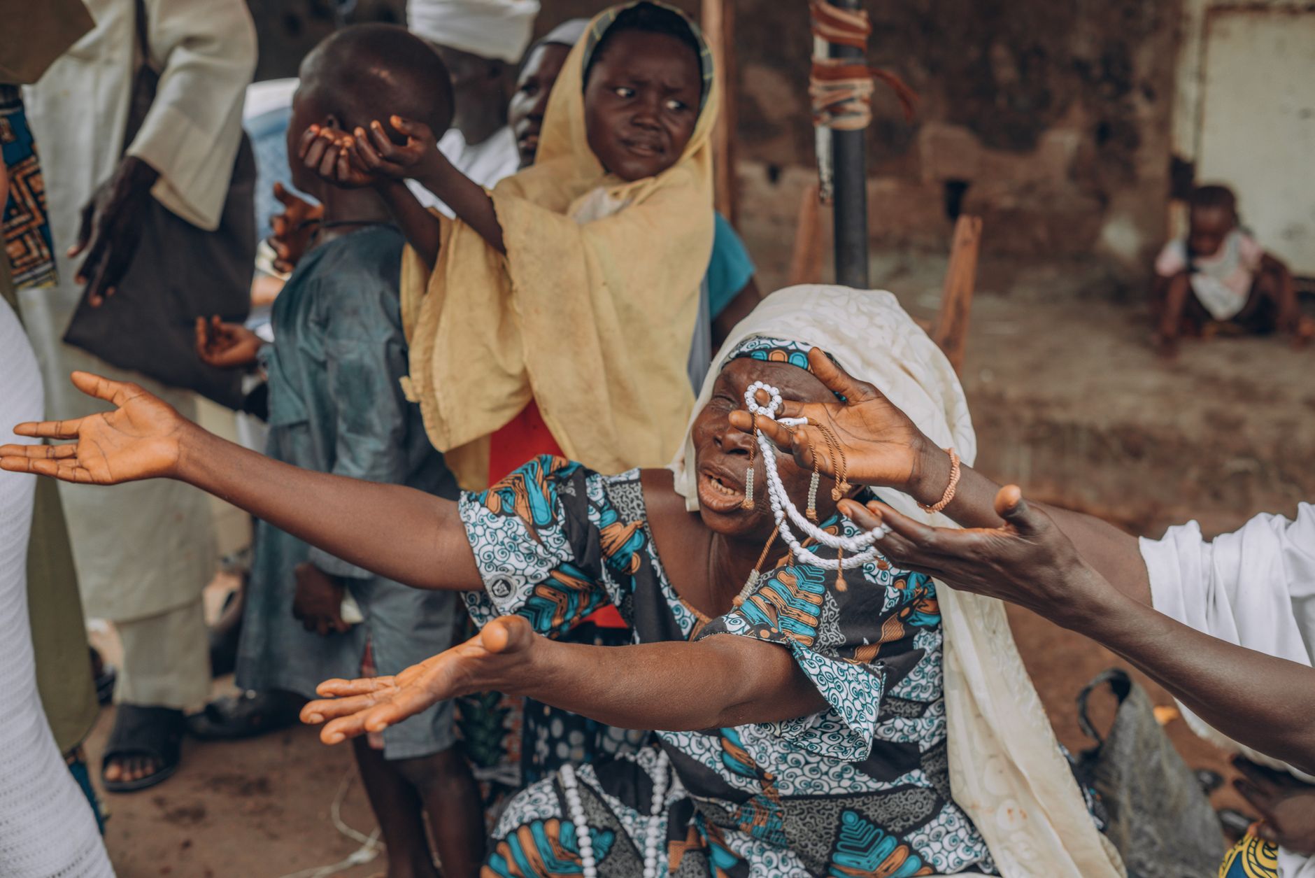 A woman expressing joy and gratitude in an African village setting surrounded by cultural elements.