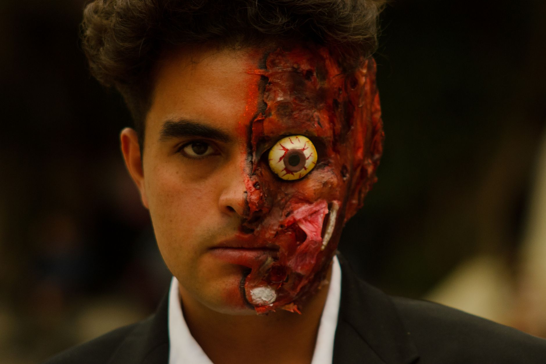 Close-up of artistic cosplay with intricate facial makeup and horned accessories outdoors.