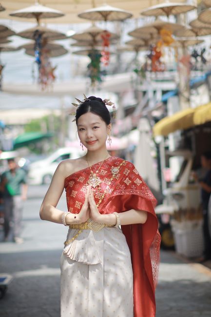 Young woman in traditional Thai costume greeting in Bangkok street market.
