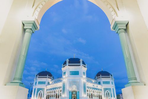 Free Beautiful view of a mosque's blue architectural design framed by arches during twilight. Stock Photo