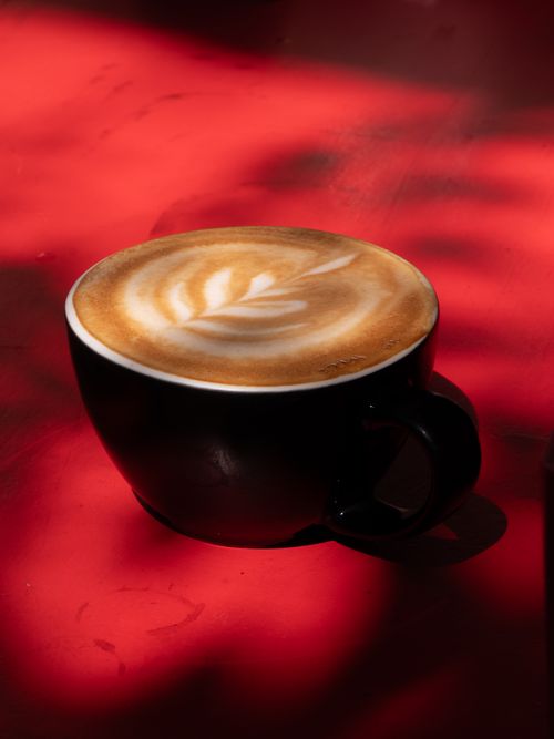 Free A beautifully crafted latte with intricate art in a black cup against a bold red background. Stock Photo