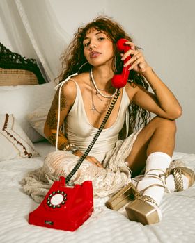Woman in retro style holding a red rotary phone in a vintage room setting.